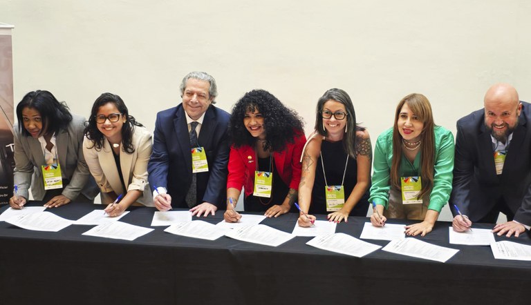 Na foto sete representantes posam assinando os documentos do evento