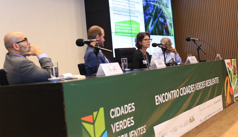 Na imagem três homens e uma mulher falando ao microfone.