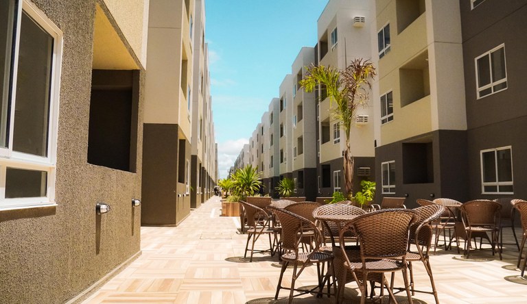 Na foto vista panorâmica do corredor de prédios das unidades habitacionais do MCMV que forma uma área de convivência