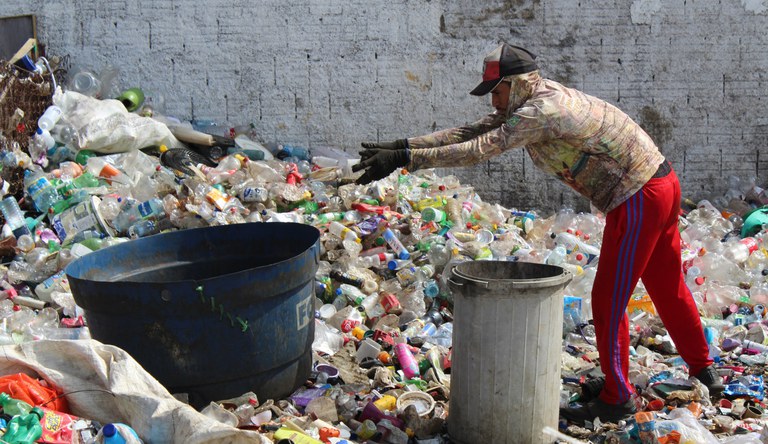 Na foto homem faz separação de garrafas plásticas para reciclagem