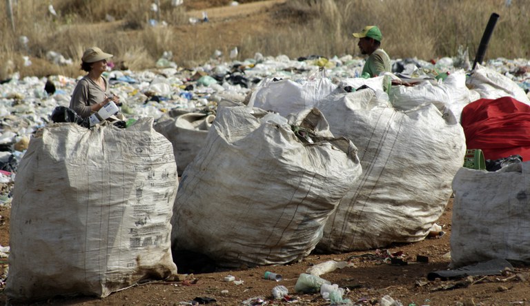 Na imagem vários sacos grandes com recicláveis e dois catadores organizando