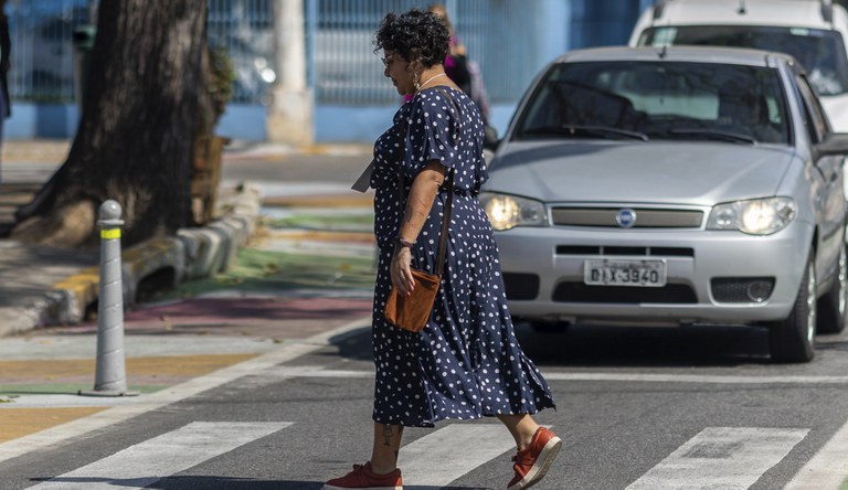 Na foto uma senhora atravessa a faixa de pedestres enquanto os carros aguardam sua passagem