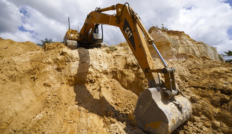 Na foto uma escavadeira no alto de uma encosta efetua trabalho de contenção.