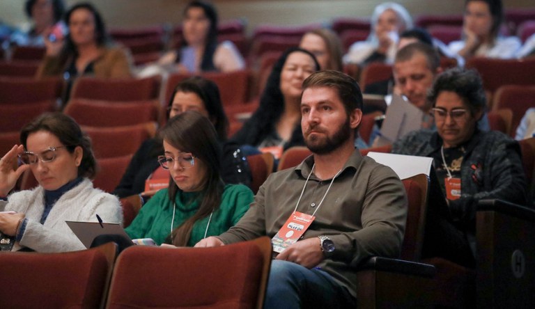 Grupo de pessoas sentadas num auditório com cadeiras vermelhas.