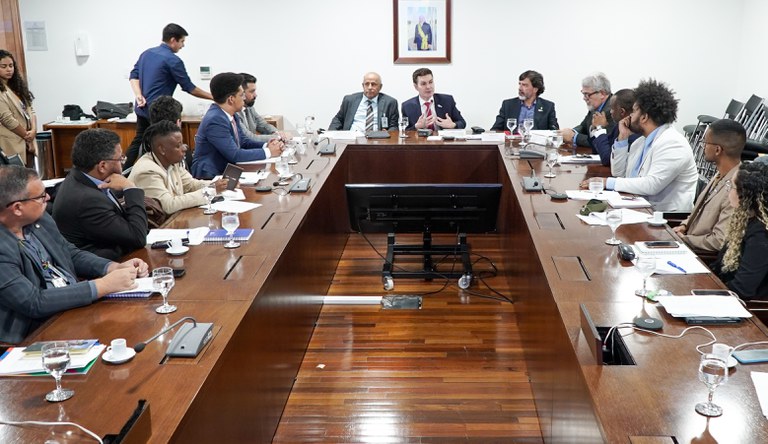 Na imagem há mulheres e homens sentados numa mesa redonda conversando sobre parceria do Ministério das Cidades e Unicef.