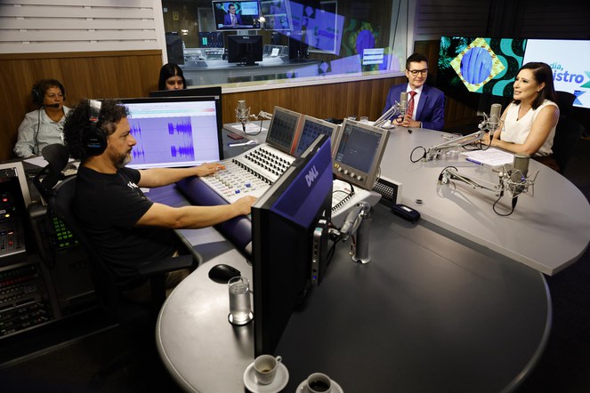 Uma mulher e um homem sentados numa mesa redonda com microfone.