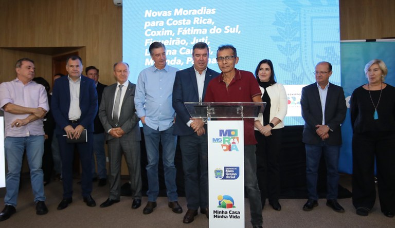 Seis homens e duas mulheres posam ao lado de um beneficiário do programa Minha Casa, Minha Vida, ao centro da imagem.