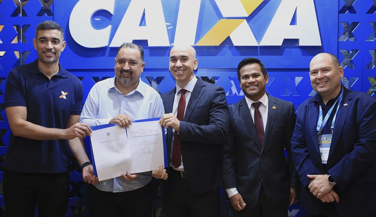 Pessoas posando com o contrato assinado com a logo da Caixa ao fundo