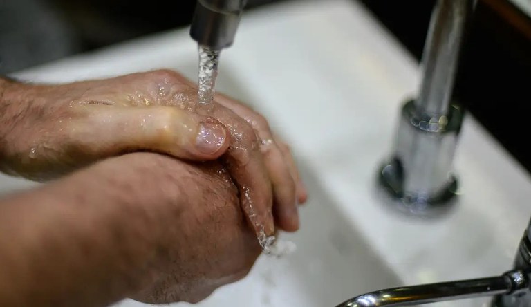Uma pessoa lavando as mãos numa torneira.