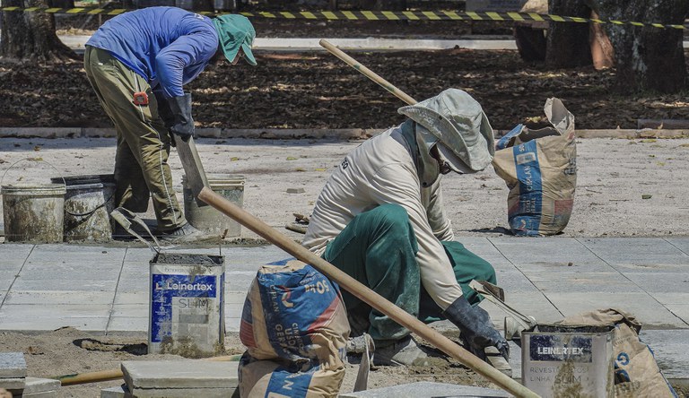 Na foto dois trabalhadores da construção civil trabalhando em uma calçada