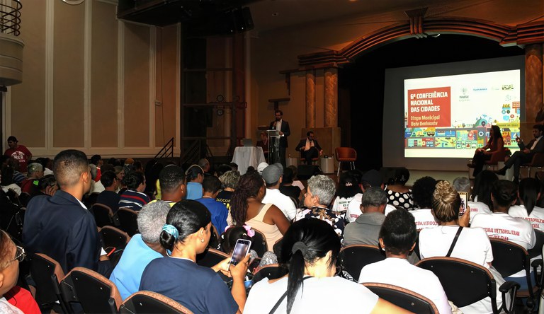 Na foto participantes da conferência assistem apresentação em um telão