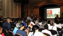 Na foto participantes da conferência assistem apresentação em um telão