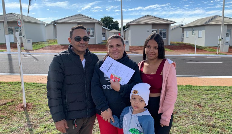 Na imagem família em frente as casas habitacionais do programa MCMV.