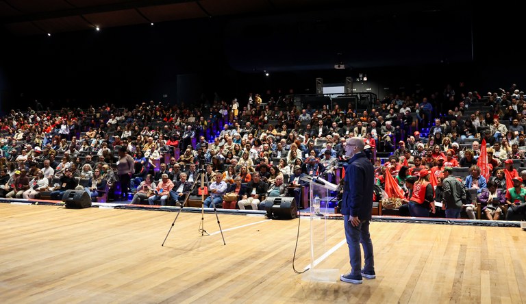 Homem no palanque e plateia de fundo.