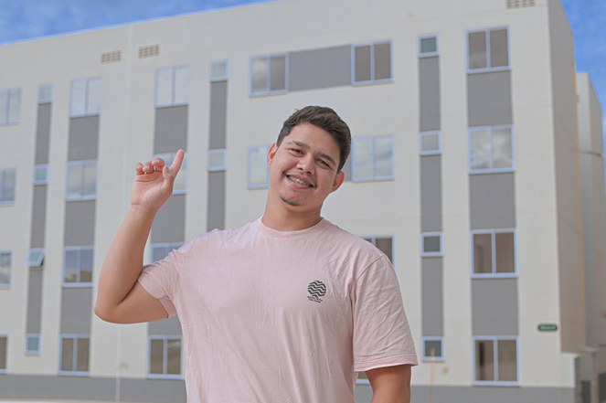 Homem sorrindo para o fotógrafo em frente a quadra poliesportiva.