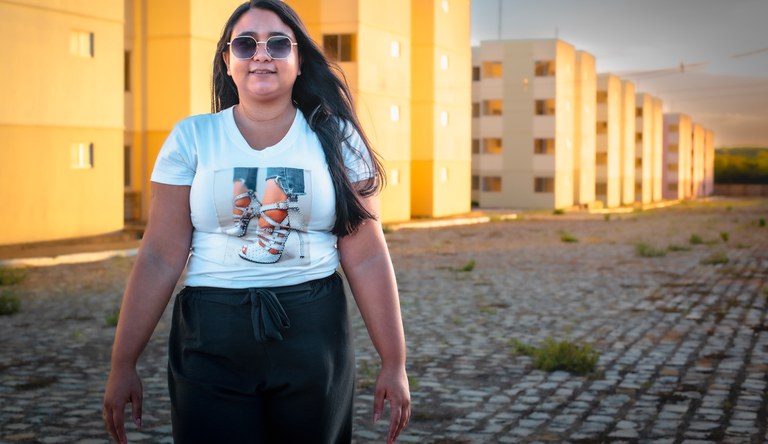 Mulher em frente de prédios do programa Minha Casa, Minha Vida