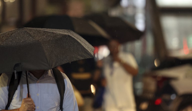 Na foto pessoas usando guarda-chuva durante temporal