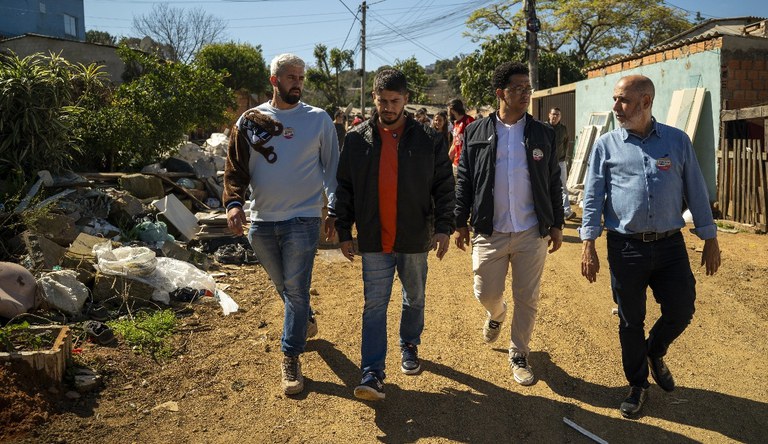 Na imagem quatro homens andando em rua sem asfalto