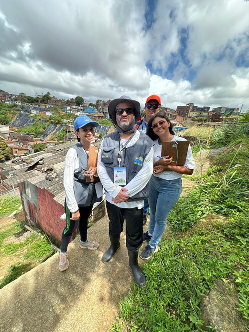 Na imagem três pessoas com jaleco de pesquisa, ao fundo comunidade pernambucana