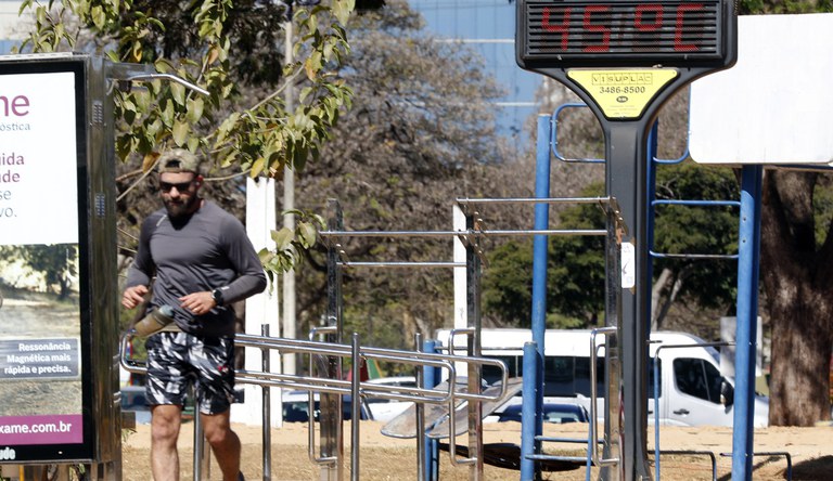 Na foto homem correndo na orla de uma praia com relógio público indicando 45 graus de temperatura