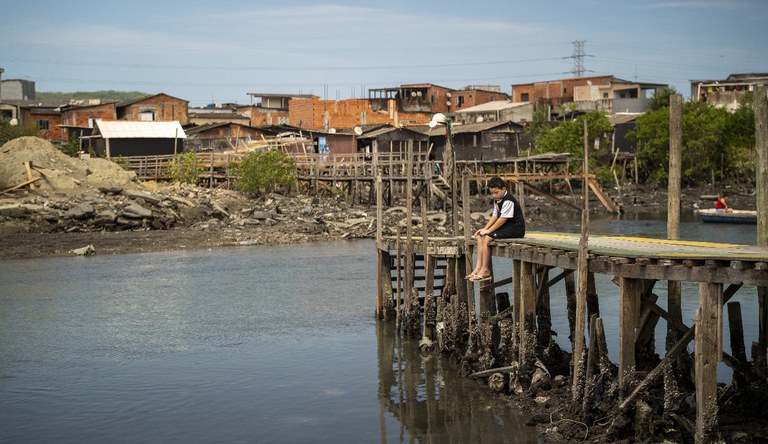Garoto sentado em ponte de madeira em frente as palafitas