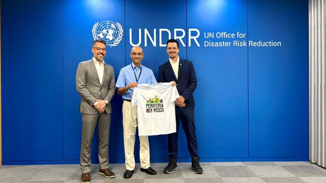 Três homens, um deles segura a camiseta do programa Periferia Sem Risco