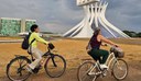 Duas pessoas andando de bicicleta em frente a catedral de Brasília