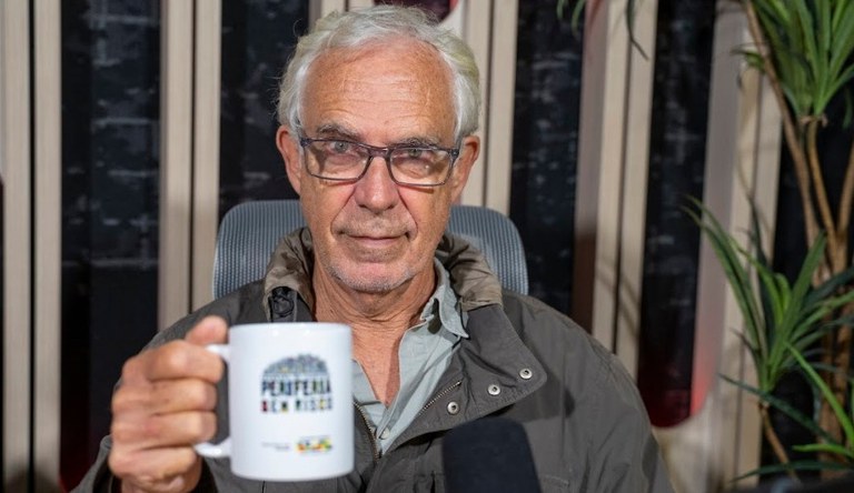 Na imagem homem sorrindo segurando uma x´ícara do programa Periferia Viva