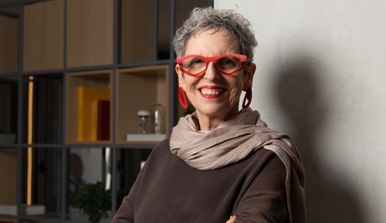 Na imagem mulher de óculos vermelho sorrindo para fotógrafo