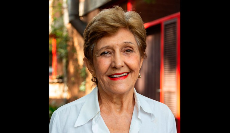 Na imagem mulher de blusa branca sorrindo para fotógrafo