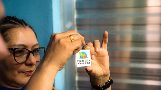 Mulher segurando um chaveiro em formato de casa escrito Minha Casa, Minha