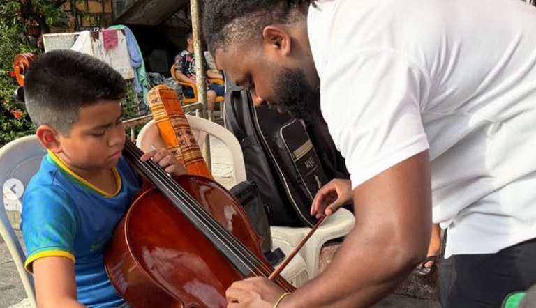 Criança sendo orientada por um professor de violoncelo
