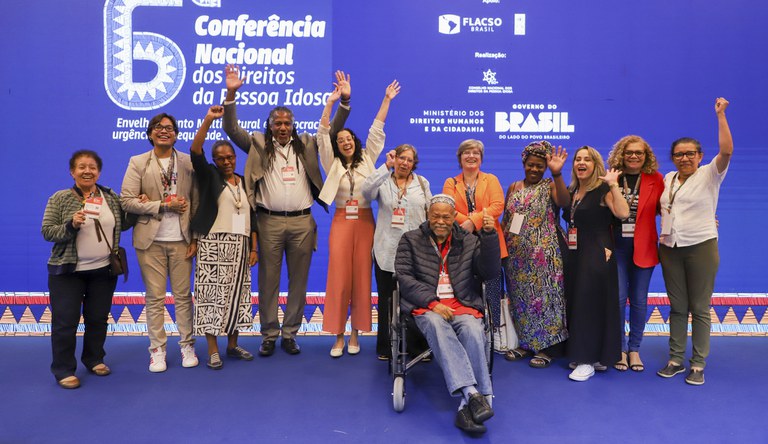 Na foto a comitiva do MCID posa para foto em frente ao banner do evento no palco