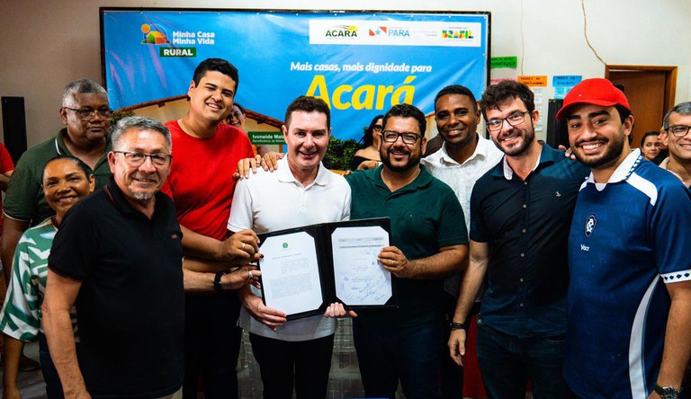 Na foto o ministro das cidades junto a autoridades e populares exibindo o documento assinado