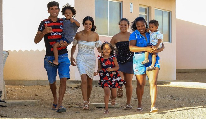 Na imagem família sorrindo em frente a casa própria