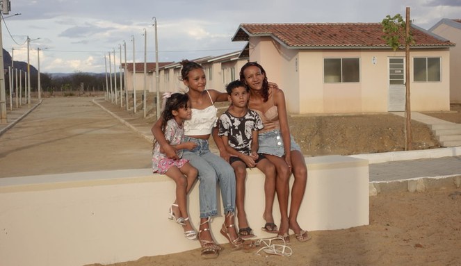 Na imagem família sentada no alpendre sorrindo para foto