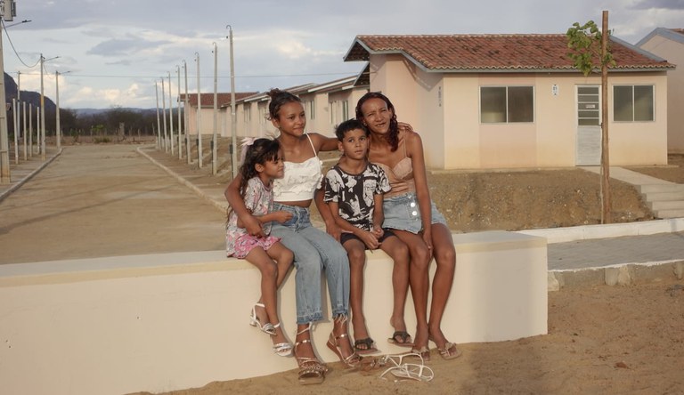 Na imagem família sentada no alpendre sorrindo para foto