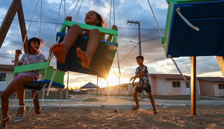 Na imagem crianças brincando no parque ao fundo por do sol