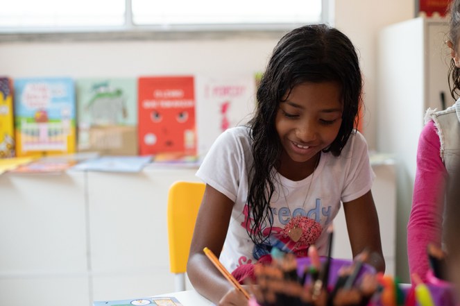 Na imagem criança lê livro na biblioteca