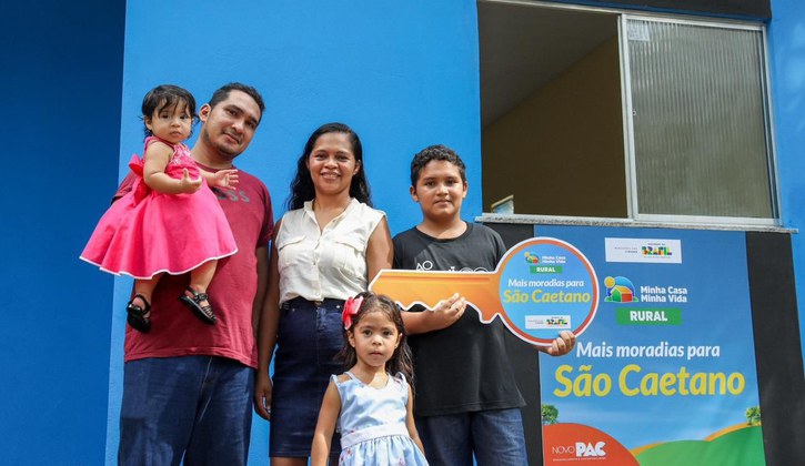 Na imagem família beneficiada do programa Minha Casa, Minha Vida Rural em frente a sua nova casa