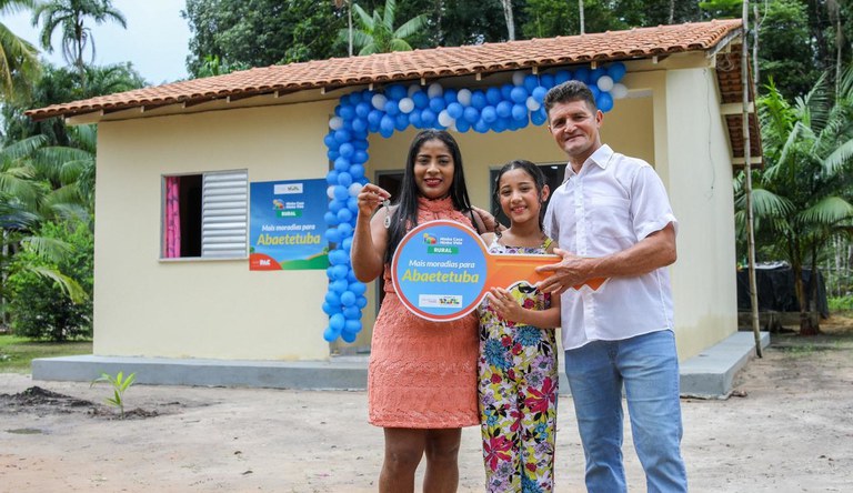 Na imagem família posa pra foto em frente a sua nova casa de alvenaria