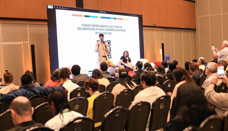 Na imagem homem apresenta dados da secretaria de periferias do ministério para plateia da 6ª CNC