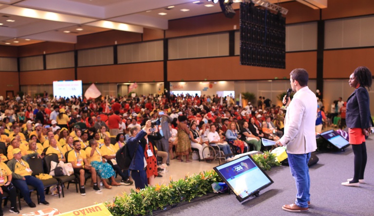 Na imagem homem falando ao microfone, ao fundo plateia da 6ª CNC