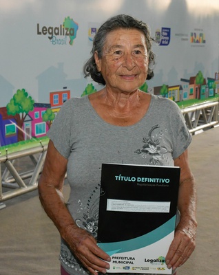 Na imagem mulher segura documento posse de casa.