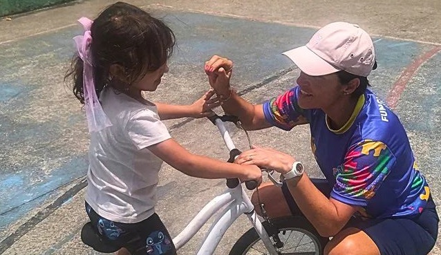 Na imagem mulher ajuda criança andar de bicicleta