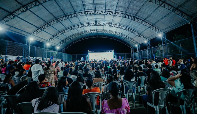 Na imagem pessoas reunidas num galpão aberto durante entrega de títulos de moradias em Pernambuco.