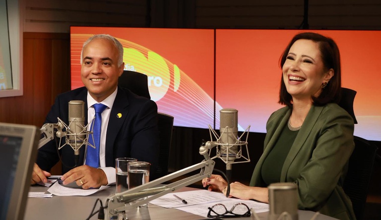 Na imagem homem e mulher no estúdio de Podcast, ao fundo banner do programa Bom dia, ministro