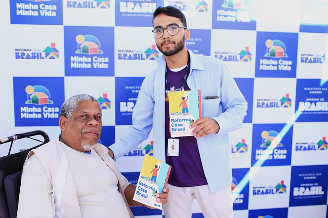 Na imagem dois homens, um deles é cadeirante posam para foto com panfleto do reforma Brasil