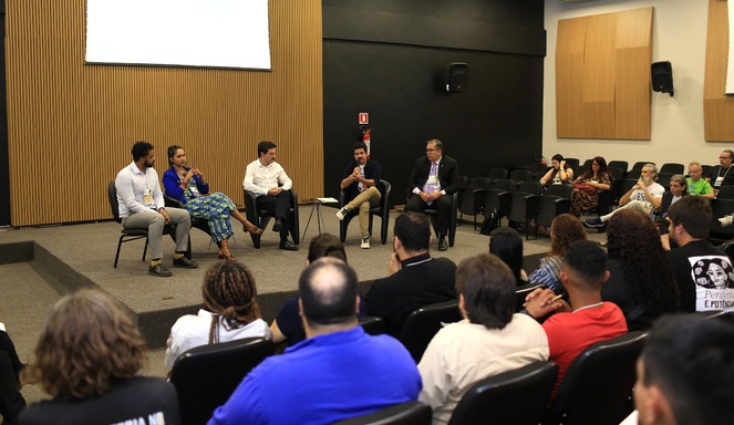 Na imagem pessoas reunidas num auditório durante palestra sobre ações nas periferias do Brasil