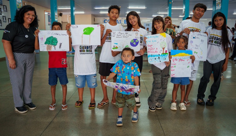 Na imagem estudantes posam para foto com cartazes pedindo cuidados ao meio ambiente